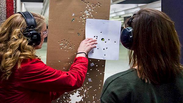 Two Female Shooters Examining their Shot Grouping on a Paper Target at an Indoor Range